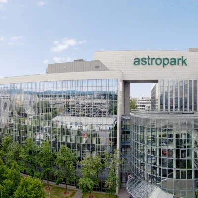 Das Bild zeigt den Haupteingang des Bürogebäudes Astropark Frankfurt mit markanter Glasfassade aus der Vogelperspektive.