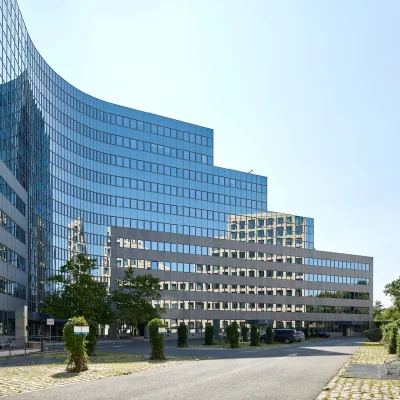 Seitenansicht des Bürogebäudes Platinum in Berlin mit Glasfassade und begrünter Zufahrt.