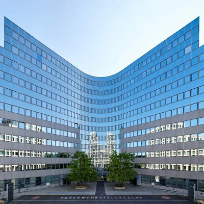Frontalansicht des Bürogebäudes Platinum in Berlin mit markanter Glasfassade und Bepflanzung im Eingangsbereich.