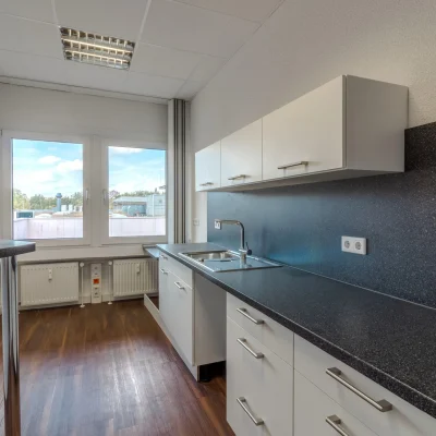 Zu sehen ist eine moderne Büroküche mit Küchenzeile, Spülbecken und Arbeitsfläche vor einem Fenster.