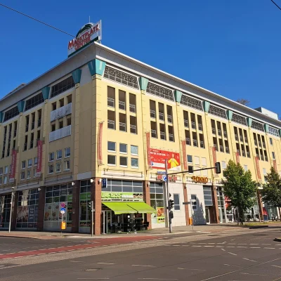 Das Bild zeigt die Straßenansicht des Marktplatz Centers in Berlin-Hellersdorf mit einem großen gelben Büro- und Geschäftsgebäude an einer Kreuzung.