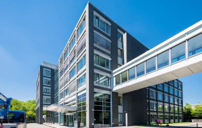 Zu sehen ist die Frontansicht eines modernen Bürogebäudes in Eschborn mit einer verglasten Verbindungsbrücke.