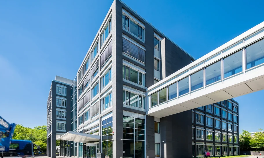 Zu sehen ist die Frontansicht eines modernen Bürogebäudes in Eschborn mit einer verglasten Verbindungsbrücke.