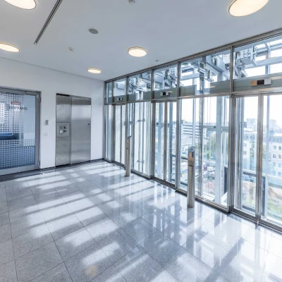 Zu sehen ist ein Flur mit Glasfront und Aufzug in einem modernen Bürogebäude mit Ausblick über die Stadt.
