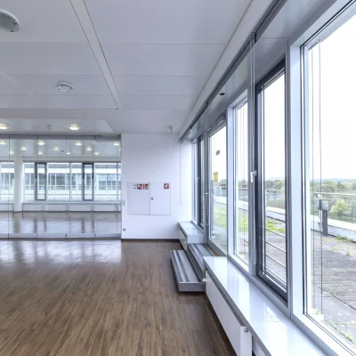 Das Bild zeigt ein leeres Büro mit großen Fensterflächen und Zugang zur Terrasse.
