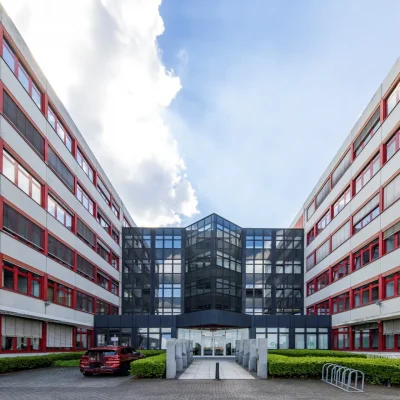 Das Bild zeigt die Frontansicht eines Bürokomplexes mit zentralem Glaseingang und symmetrisch angeordneten Gebäuden.