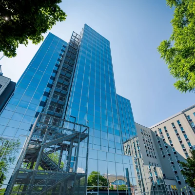 Ein modernes Bürohochhaus in Frankfurt mit verspiegelter Glasfassade spiegelt den Himmel und umliegende Gebäude wider.