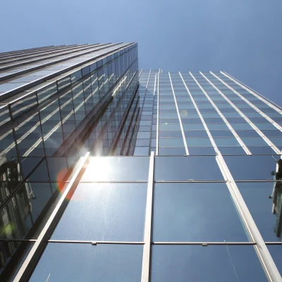 Ein modernes Bürohochhaus mit verspiegelter Glasfassade ragt in den Himmel und reflektiert die Wolken und umliegenden Gebäude.