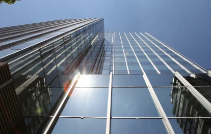 Ein modernes Bürohochhaus mit verspiegelter Glasfassade ragt in den Himmel und reflektiert die Wolken und umliegenden Gebäude.
