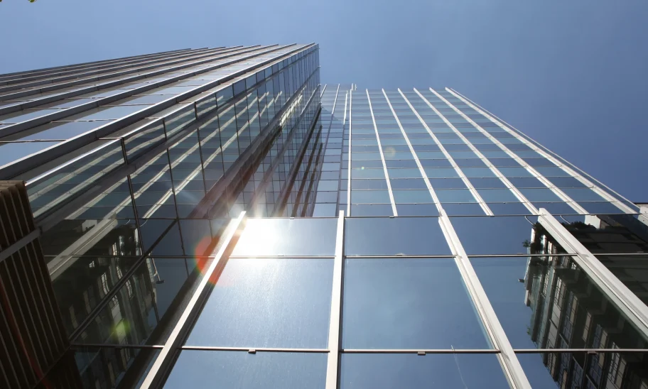 Ein modernes Bürohochhaus mit verspiegelter Glasfassade ragt in den Himmel und reflektiert die Wolken und umliegenden Gebäude.