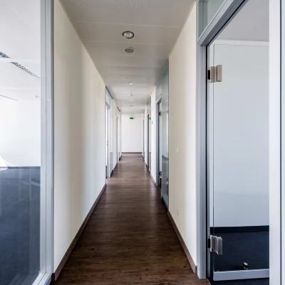 Das Bild zeigt einen langen Büroflur im HAT64 Frankfurt mit Holzboden, Glastüren und modernen Bürozugängen.