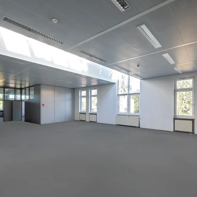 Ein leerer, heller Büroraum mit großen Fenstern und moderner Decke mit Beleuchtung.