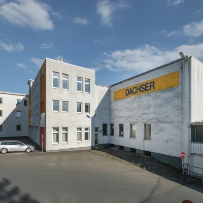 Außenansicht eines Bürogebäudes mit Dachser-Beschriftung, umgeben von Asphaltflächen und Einfahrt.