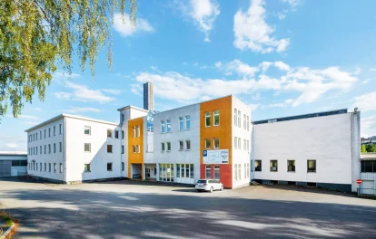 Ein modernes Bürogebäude mit markanter orangefarbener Fassade und angrenzendem Parkplatz bei sonnigem Wetter.