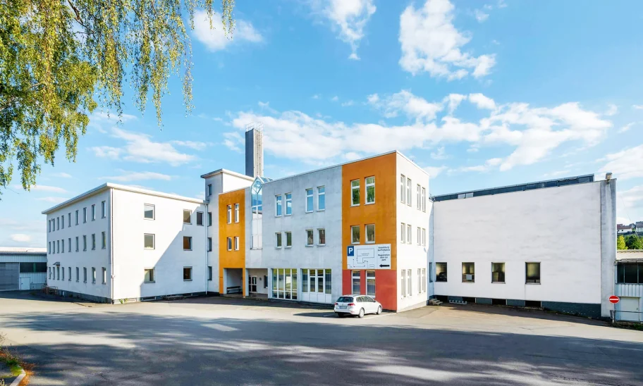 Ein modernes Bürogebäude mit markanter orangefarbener Fassade und angrenzendem Parkplatz bei sonnigem Wetter.