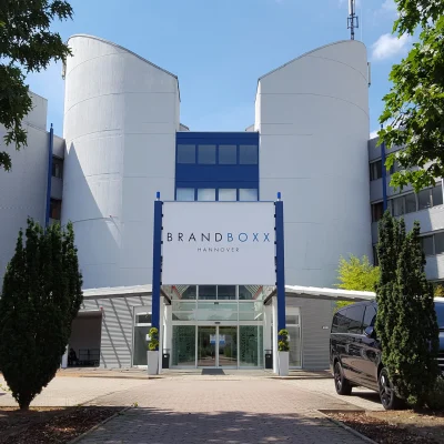Die Außenansicht des Bürogebäudes Brandboxx in Hannover zeigt den Haupteingang mit Glasfassade und angrenzender Parkanlage.