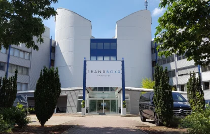 Die Außenansicht des Bürogebäudes Brandboxx in Hannover zeigt den Haupteingang mit Glasfassade und angrenzender Parkanlage.