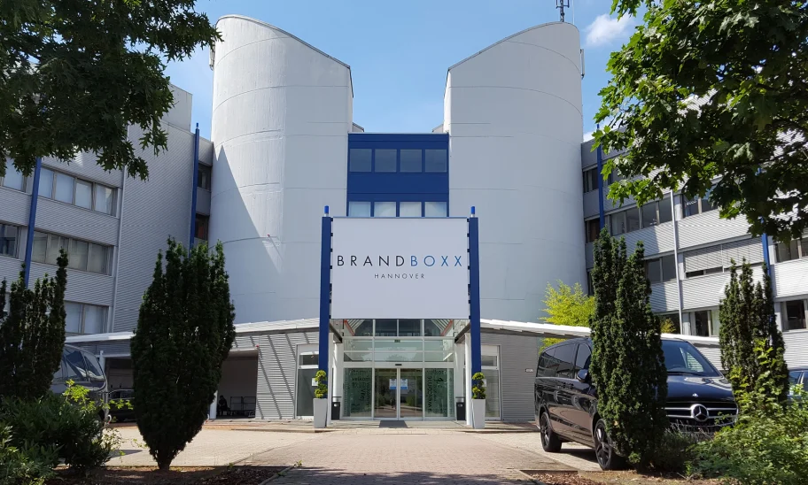 Die Außenansicht des Bürogebäudes Brandboxx in Hannover zeigt den Haupteingang mit Glasfassade und angrenzender Parkanlage.