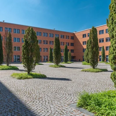 Das Bild zeigt den gepflasterten Innenhof des Kontorhofs Teltow mit symmetrischer Bepflanzung und umrahmenden Bürogebäuden.