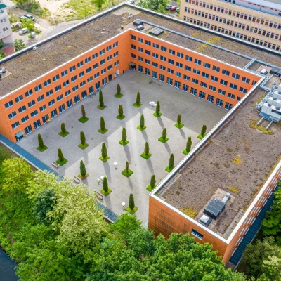Das Bild zeigt eine schräge Luftaufnahme eines Bürogebäudes mit strukturiert bepflanztem Innenhof in Teltow bei Berlin.
