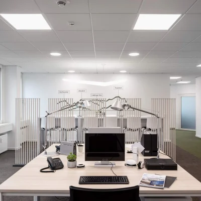 Moderner Arbeitsplatz mit Schreibtisch, Lampen und Sichttrennwänden entlang eines Flurs in einem Münchner Büro.