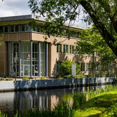 Abgebildet ist ein Bürohaus mit Glasfassade, das sich in einem Teich im begrünten Gewerbepark spiegelt.