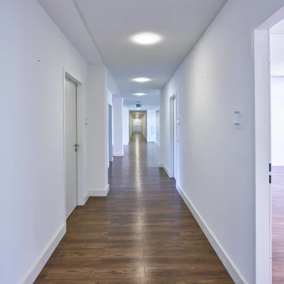 Langer, heller Büroflur mit Holzfußboden und Zugang zu mehreren Räumen links und rechts.