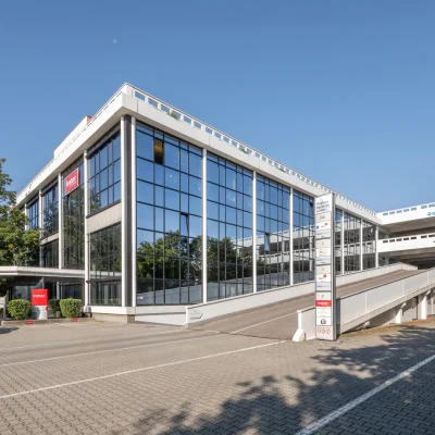 Ein moderner Gebäudekomplex mit Anfahrtsrampe und verspiegelter Glasfassade in urbaner Umgebung.
