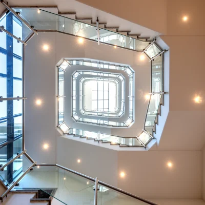 Ein mehrstöckiges Treppenhaus mit Glasgeländern und stimmungsvoller Beleuchtung von unten fotografiert.
