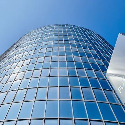 Abgebildet ist die aufsteigende Glasfassade des Platinum Office Hochhauses in Berlin mit markantem Schriftzug vor blauem Himmel.