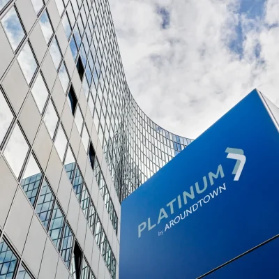 Glasfassade des Platinum Office am Sachsendamm in Berlin mit blauer Platinum-by-Aroundtown-Stele vor Wolkenhimmel