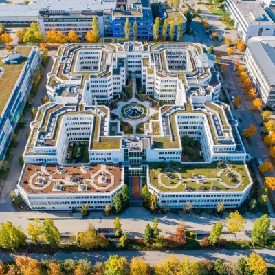 Die Luftaufnahme zeigt einen großen Bürogebäudekomplex mit begrünten Dachterrassen inmitten eines Gewerbegebiets.