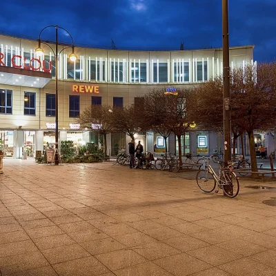 Beleuchtete Nachtansicht des Einkaufszentrums „Der Clou“ mit REWE und umliegenden Geschäften.