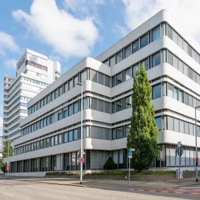 Straßenansicht des Bürogebäudes mit Hochhaus im Hintergrund und Baumbestand