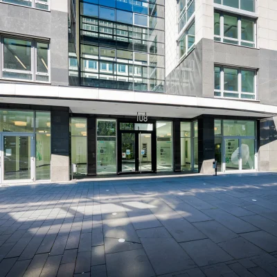 Das Bild zeigt den Haupteingang eines modernen Bürogebäudes mit Glasfassade in Frankfurt.