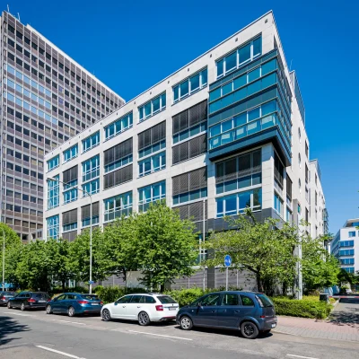 Das Bild zeigt ein modernes Bürohochhaus in Frankfurt mit Glasfassade und benachbarter Hochhausarchitektur.