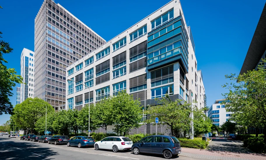 Das Bild zeigt ein modernes Bürohochhaus in Frankfurt mit Glasfassade und benachbarter Hochhausarchitektur.