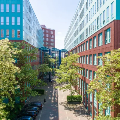 Der Innenhof eines modernen Bürokomplexes in Berlin mit roten Fassaden, Glasverbindungen und grünen Bäumen.