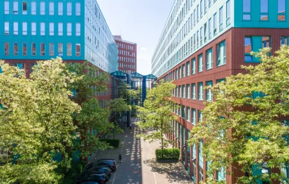 Der Innenhof eines modernen Bürokomplexes in Berlin mit roten Fassaden, Glasverbindungen und grünen Bäumen.