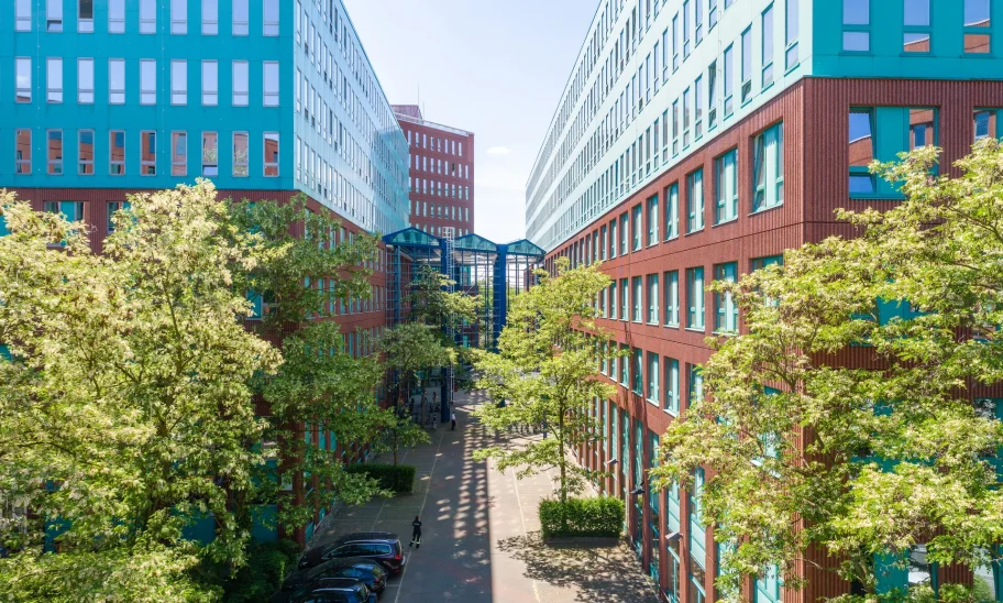 Der Innenhof eines modernen Bürokomplexes in Berlin mit roten Fassaden, Glasverbindungen und grünen Bäumen.