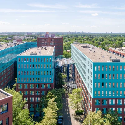 Luftaufnahme eines großen Büro- und Gewerbekomplexes in Berlin mit mehreren Gebäuden und grüner Umgebung.