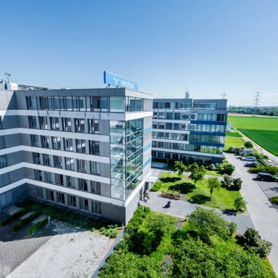 Das Bild zeigt das moderne Bürogebäude Trevista in Eschborn aus der Luftperspektive mit Glasfassade, Begrünung, Innenhof und angrenzenden Feldern.