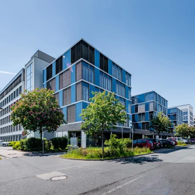 Das Bild zeigt die Rückansicht des Trevista-Bürokomplexes in Eschborn mit Parkplätzen und mehreren Gebäudeteilen.