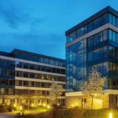 Bürogebäude-Ensemble mit Glasfassade und beleuchtetem Vorplatz in der Abenddämmerung