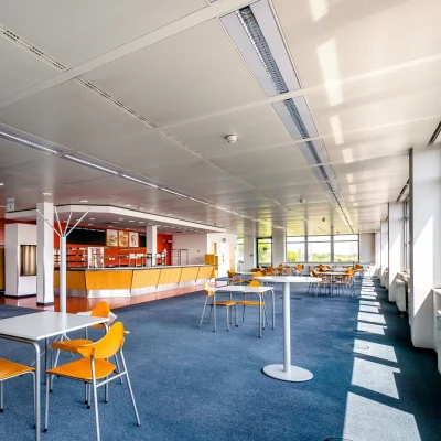 Helle Kantine im Bürogebäude mit großen Fenstern, Tischen und Stühlen.