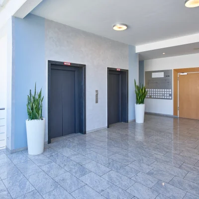 Das Bild zeigt das helle Foyer eines modernen Bürogebäudes in Ismaning mit zwei Aufzügen, Pflanzen und einem Eingangsbereich mit Doppeltüren.
