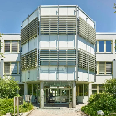 Auf dem Bild ist der Haupteingang des Type1 Office Gebäudes in Ismaning mit Glasfassade, moderner Architektur und umliegender Begrünung zu sehen.