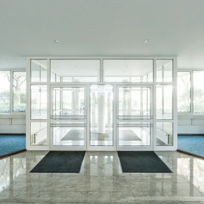 Das Bild zeigt die moderne, lichtdurchflutete Lobby eines Bürogebäudes in Ismaning mit Glasfront und dekorativen Pflanzen in weißen Töpfen.