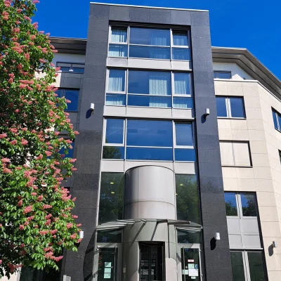 Zu sehen ist der Haupteingang eines Bürogebäudes in Bonn mit blühendem Baum und moderner Glasfassade.