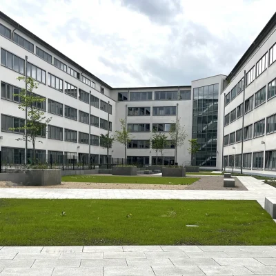 Zu sehen ist ein weitläufiger Innenhof eines Bürokomplexes mit gepflegter Grünfläche und umliegender Fensterfassade.
